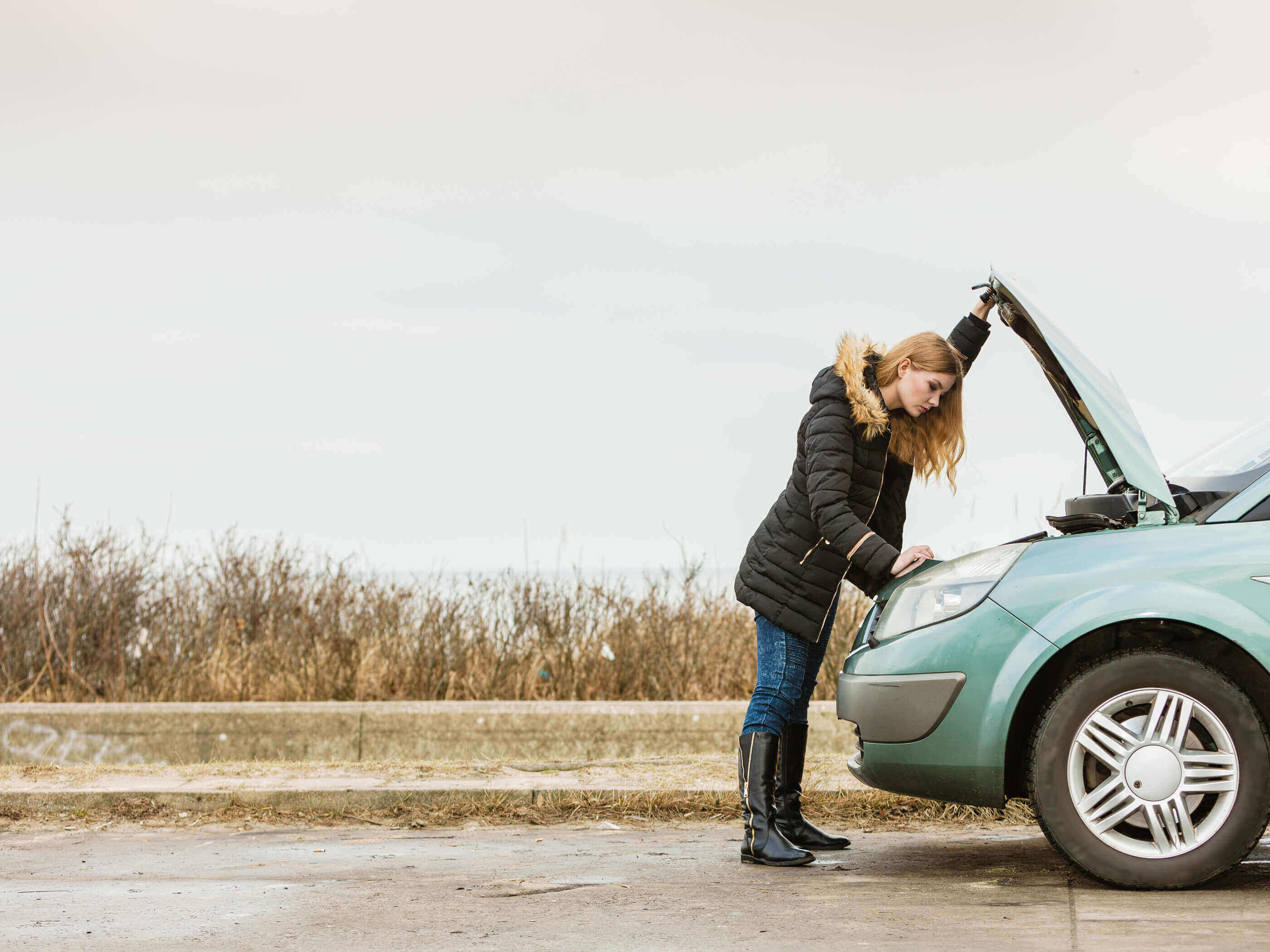 A woman looking under the bonnet of her car in a field